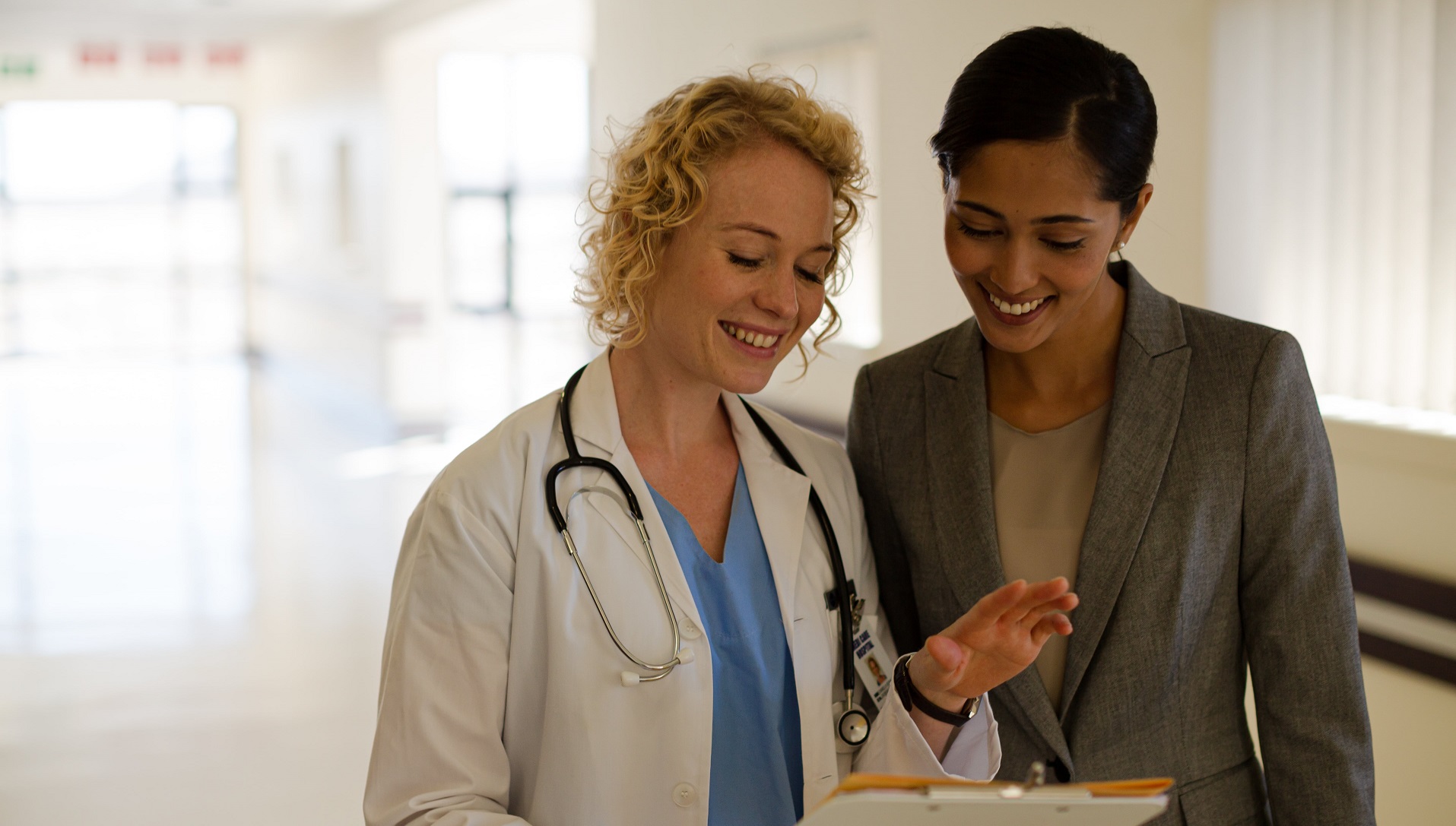 A doctor and a woman in business attire talk in hospital hallway