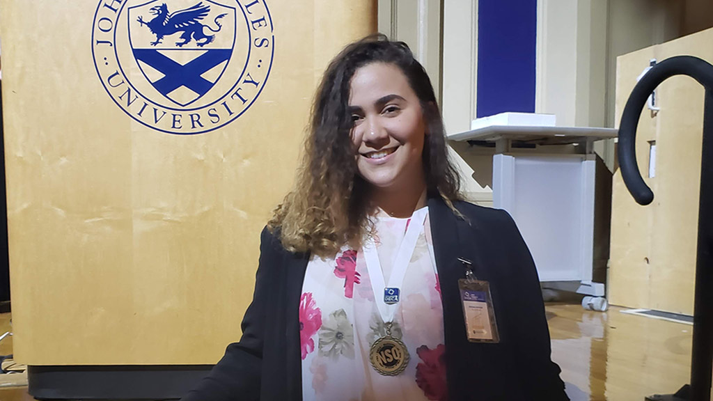 Denisses Cortorreal '20 posing in front of JWU podium