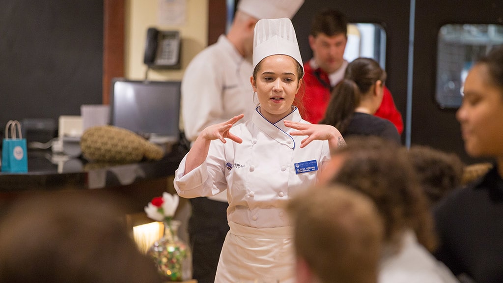 photo of a woman dressed in chef whites presenting to a group of people