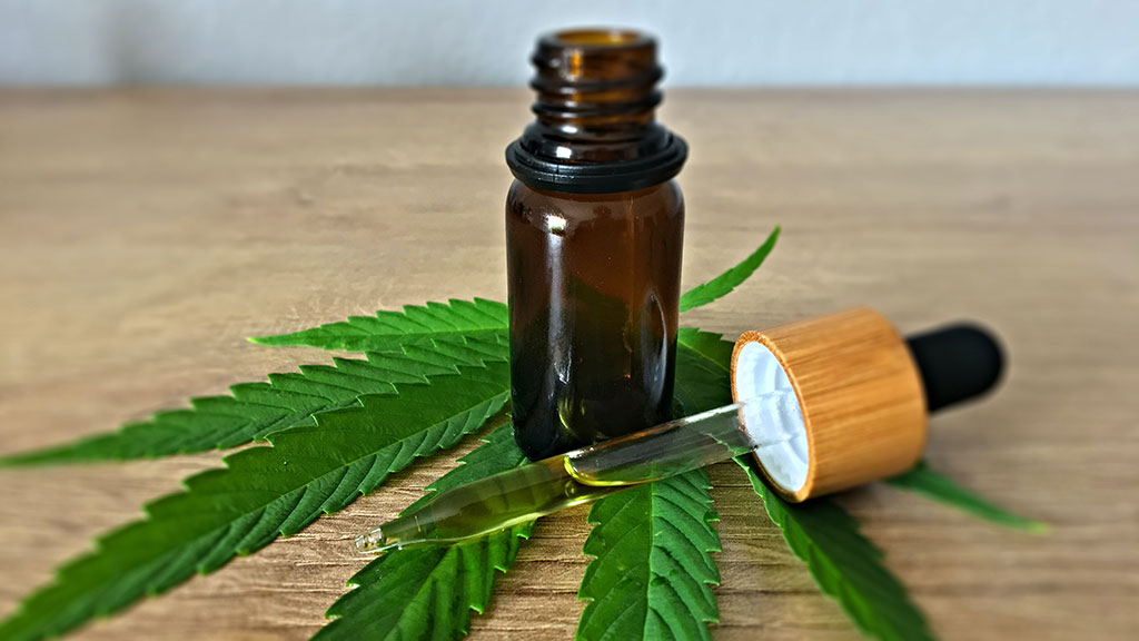 A vial and dropper full of CBD oil on top of a cannabis leaf