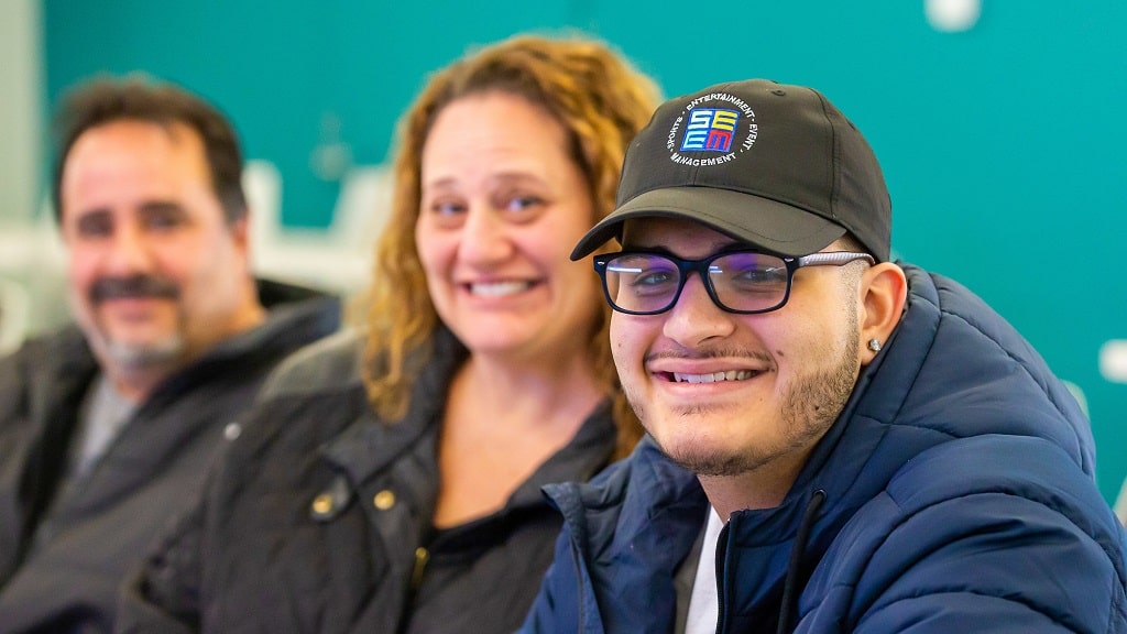 Male student in hat smiles with family in background