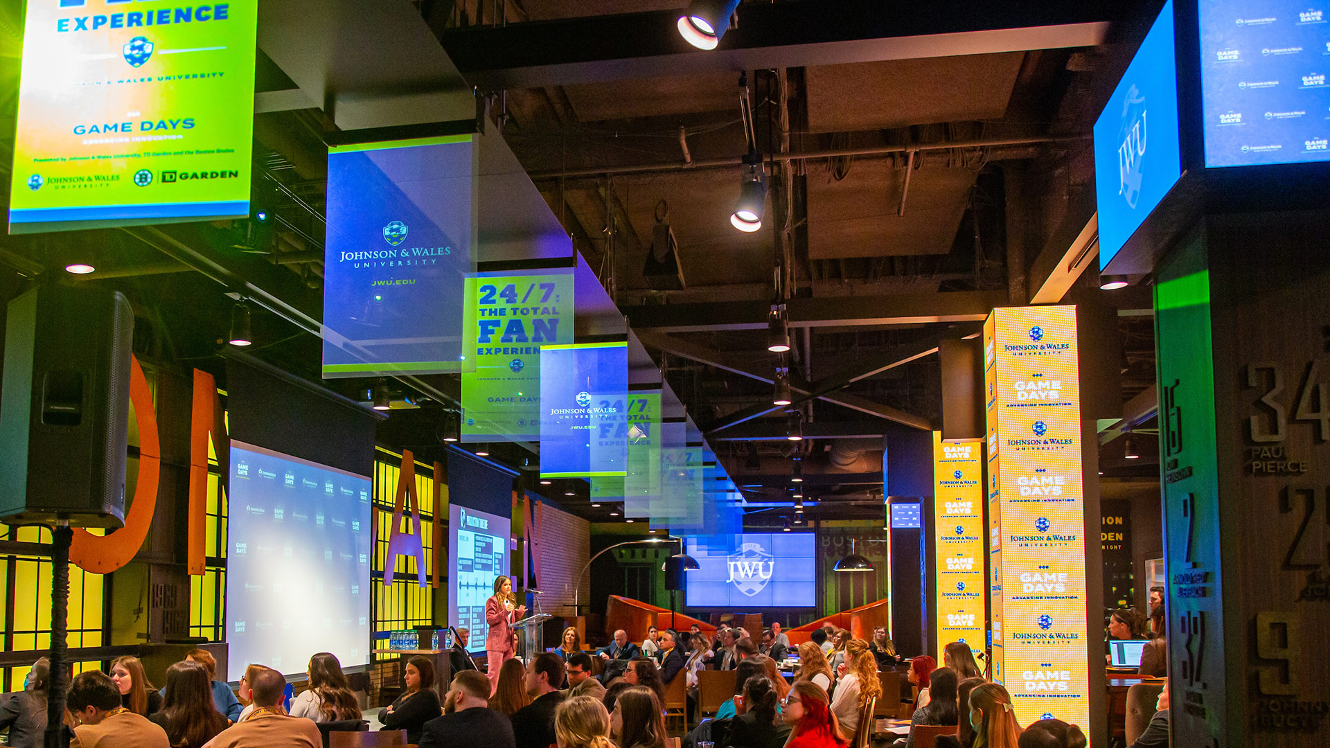 TD Gardens Legends restaurant with JWU signage and a crowd watching a person speak on the stage.