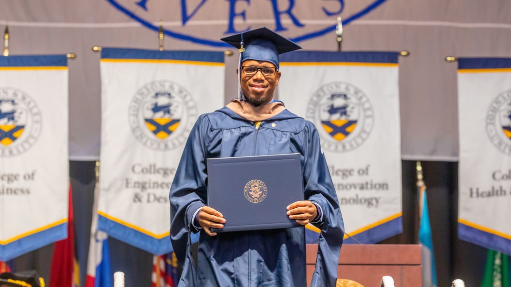 New grad standing in the center of the Commencement stage in academic regalia.