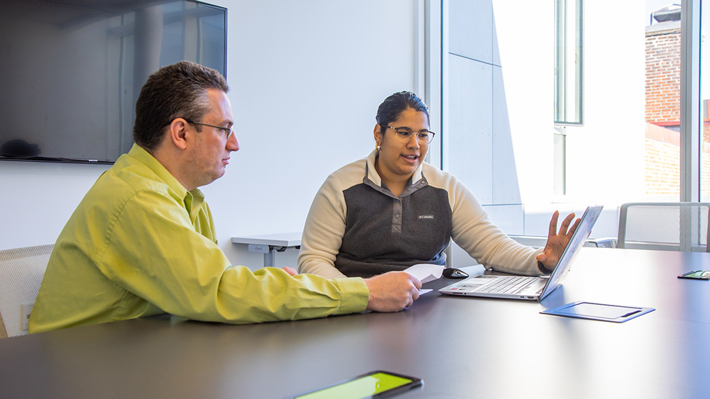 A student talking with an advisor while looking at a laptop.