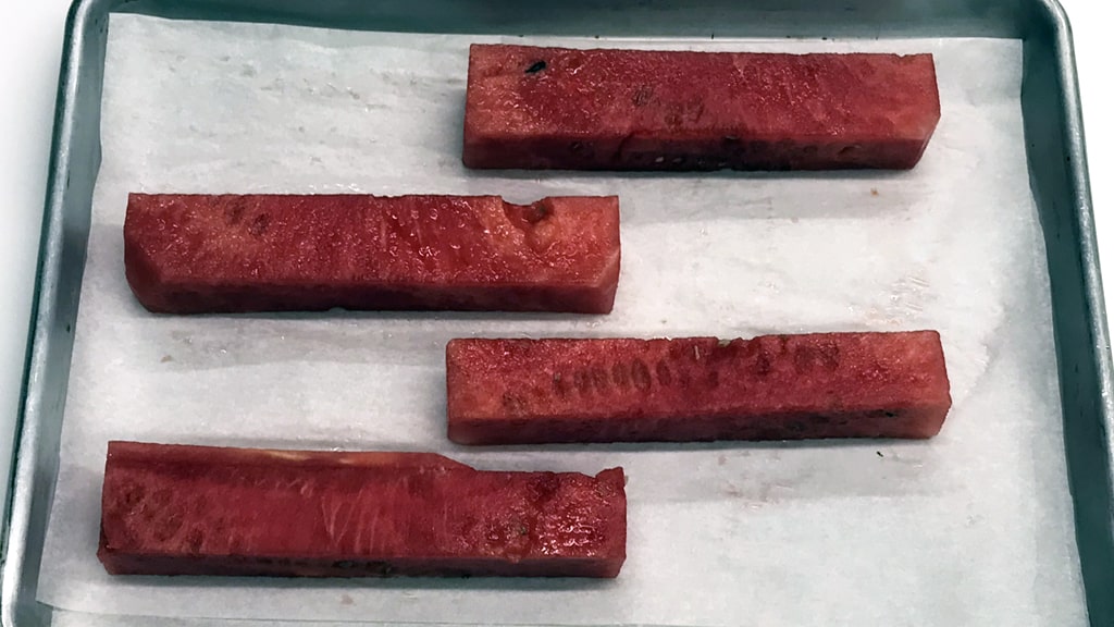 Cut planks of watermelon on a parchment-lined sheet, ready to be baked.