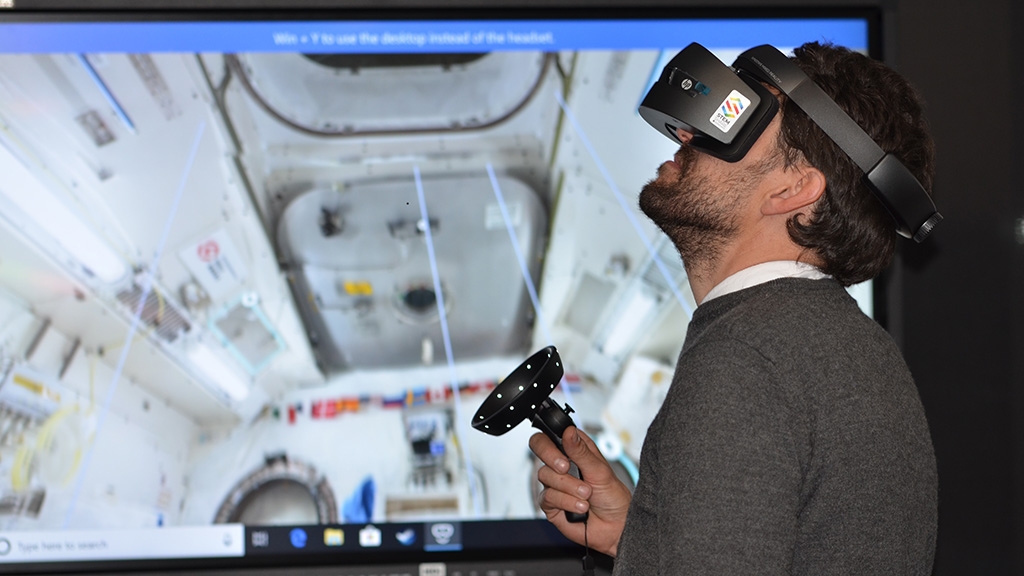 A man using a virtual reality headset with a screen behind him.