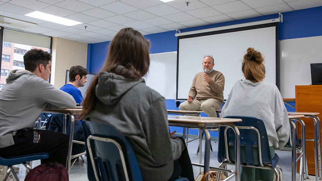 Students sitting at desks looking at a professor talking.