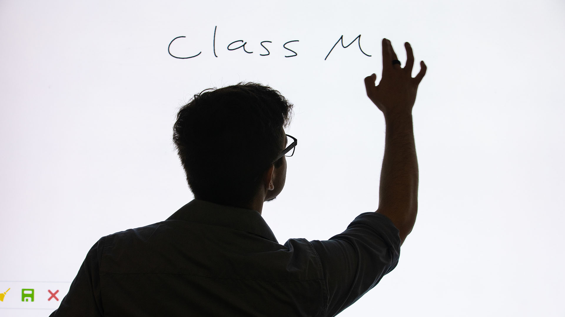 a photo of Jae Grenier in shadow as he handwrites code on a large lit screen