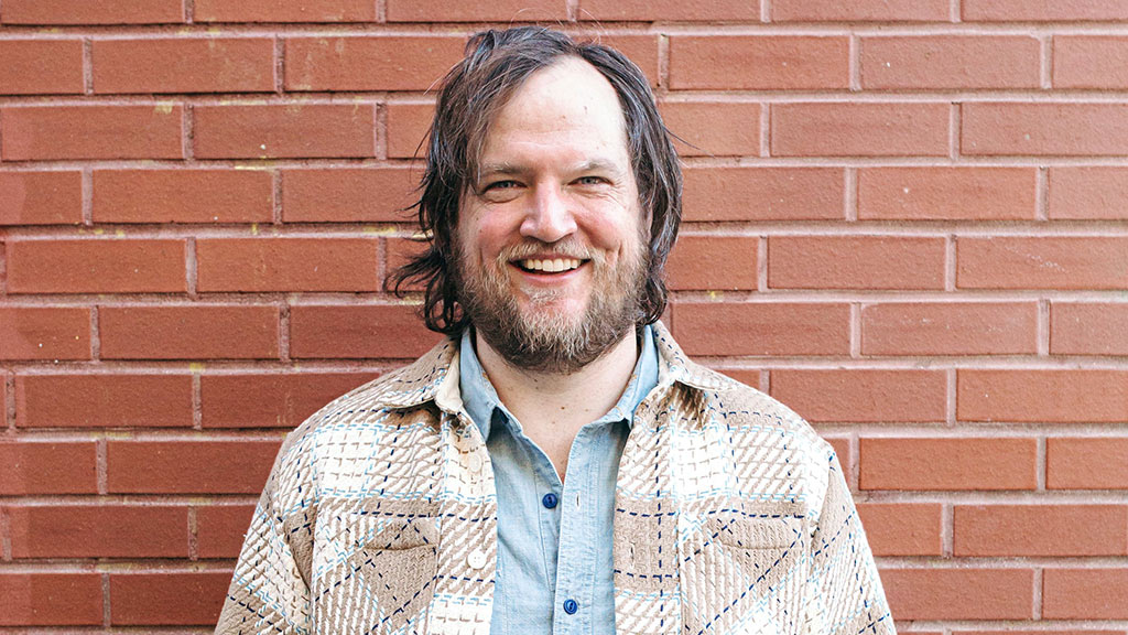 photo of Ben Sukle '08 smiling while posing against a brick wall