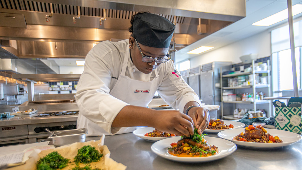 a photo of Gabby Smith adding the final garnishes to plates of food on a kitchen counter