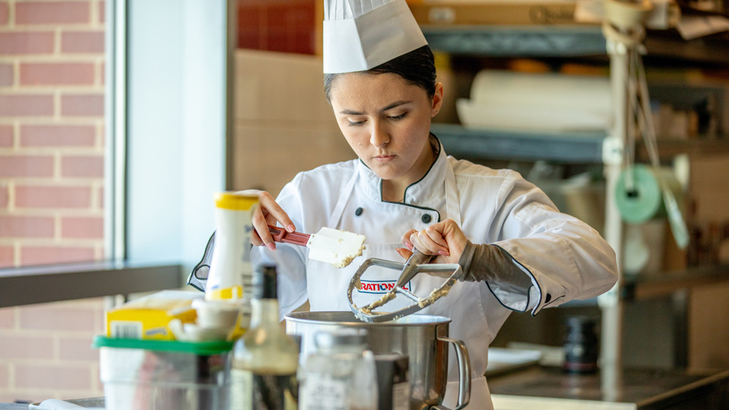 photo of Piper McAloon scraping meringue from a mixer with a spatula