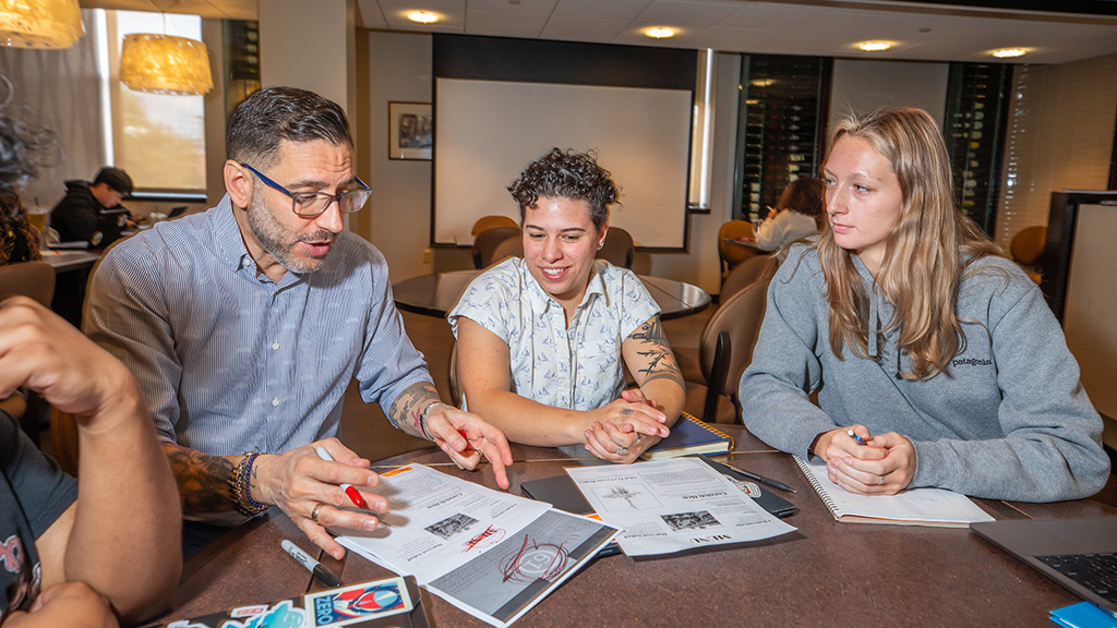 JWU student Rence Loboncz working with a professor and two other students sitting while sitting at a table in Bistro 61