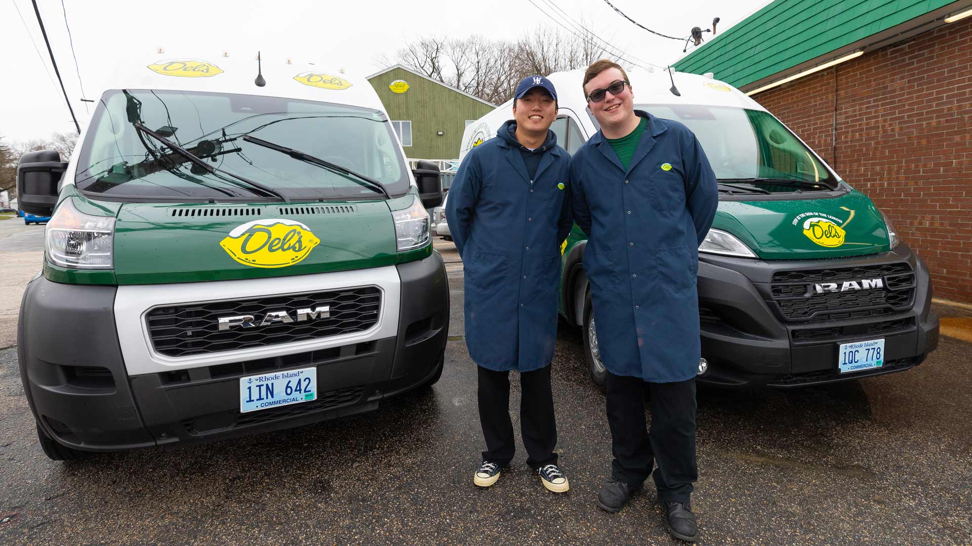 photo of Sang Hoon Chae ’23 and Caleb Atkinson ’24 posing in front of two Del’s delivery trucks in a parking lot