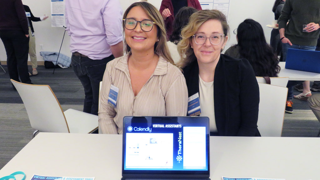 photo of Briana Seippel ’25 M.S. and Shauna Bienvenue ’25 M.S. smiling as they sit at a table at the 2024 student symposium