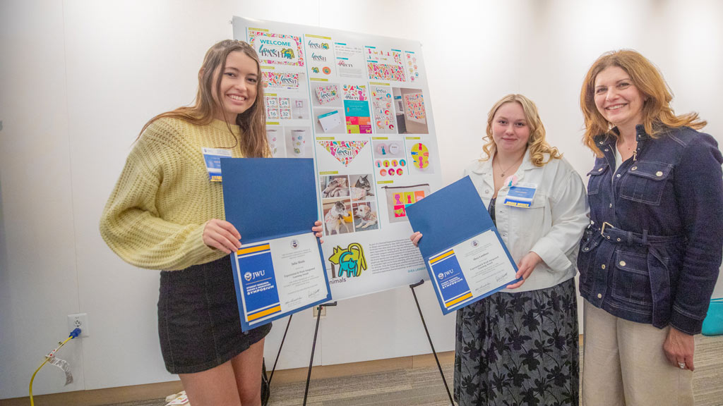 photo of Julia Shiels ’24, Shea Lambert ’24 and JWU Providence Campus President Marie Bernardo-Sousa posing in front of a project display