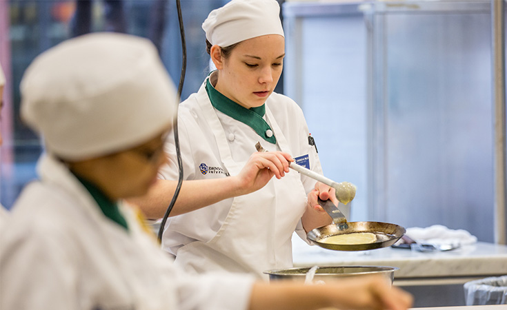 A focused student working in a culinary lab, wearing JWU chef whites.