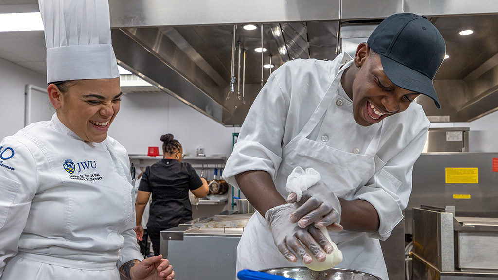 Student and chef instructor laugh as the student makes mozzarella