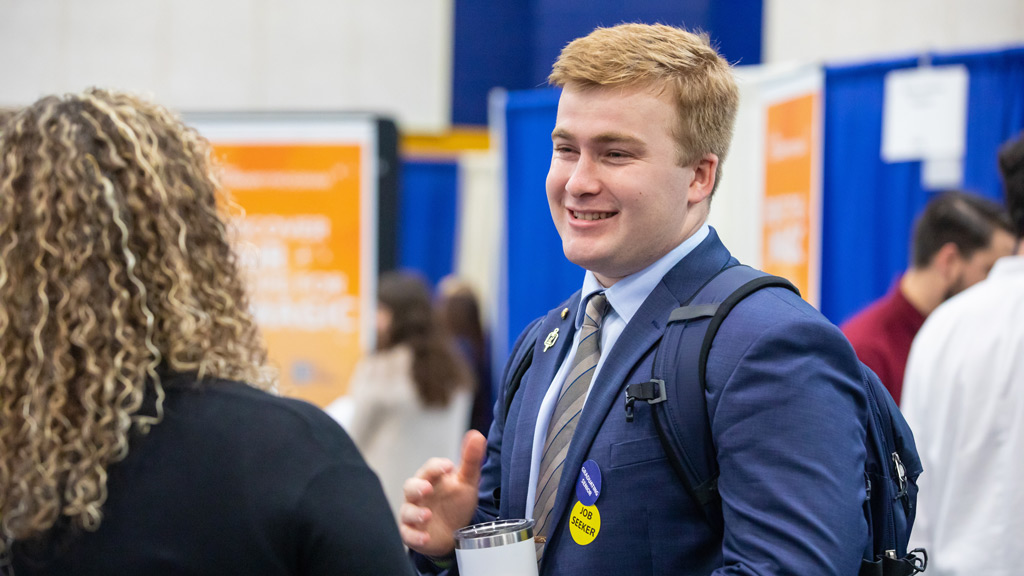 candid photo of a young man wearing a "job seeker" sticker chatting with a potential employer