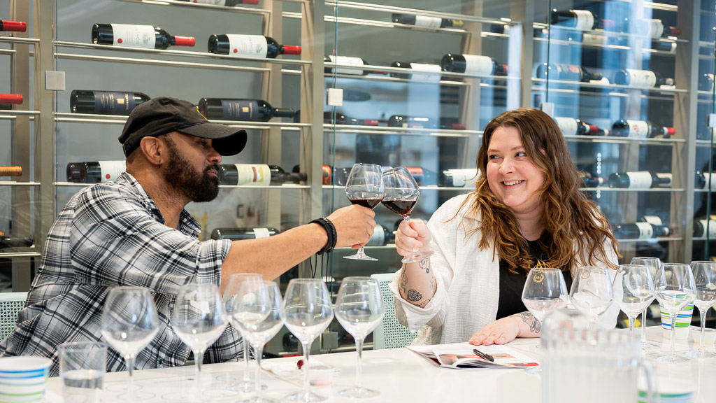 two participants in a JWU Kitchen Academy wine education class clink glasses before sipping
