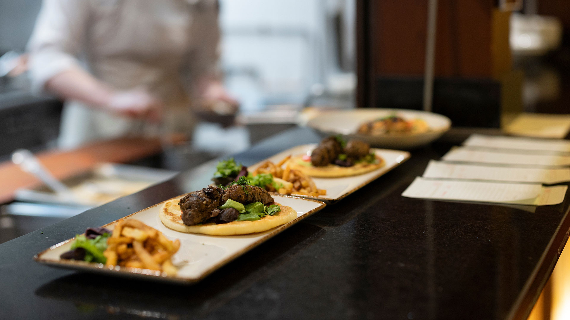 Closeup of plates of lamb kofta line the pass before service.