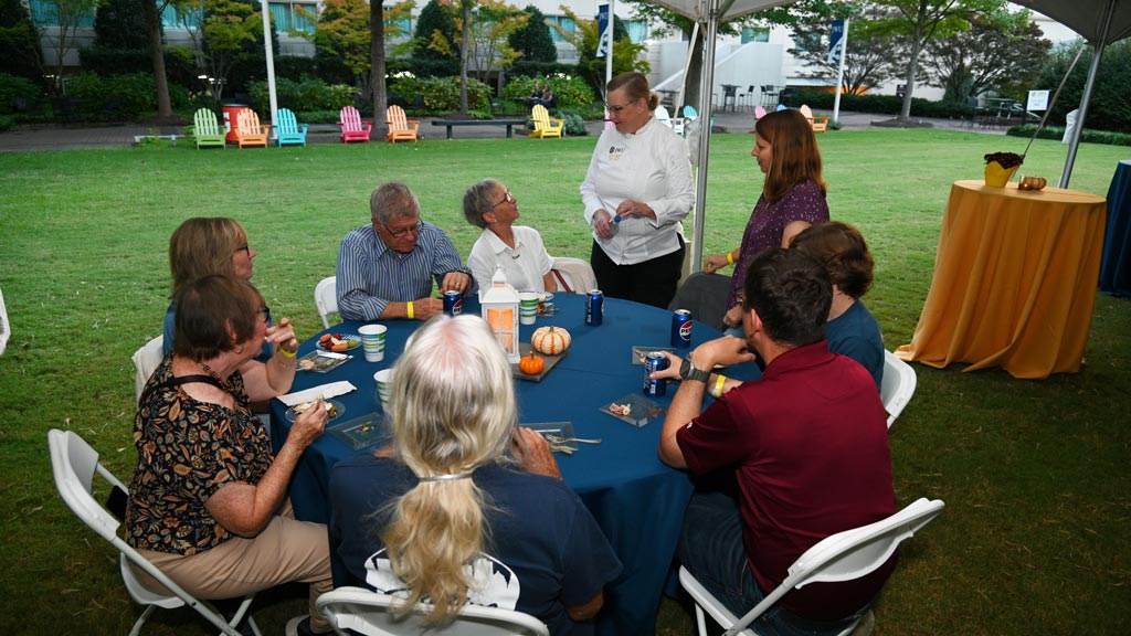 Group of people sitting at table talking to a chef