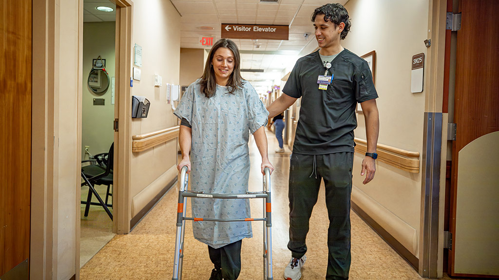 Josh Zangerle '25 helps a patient walk down a hospital hallway