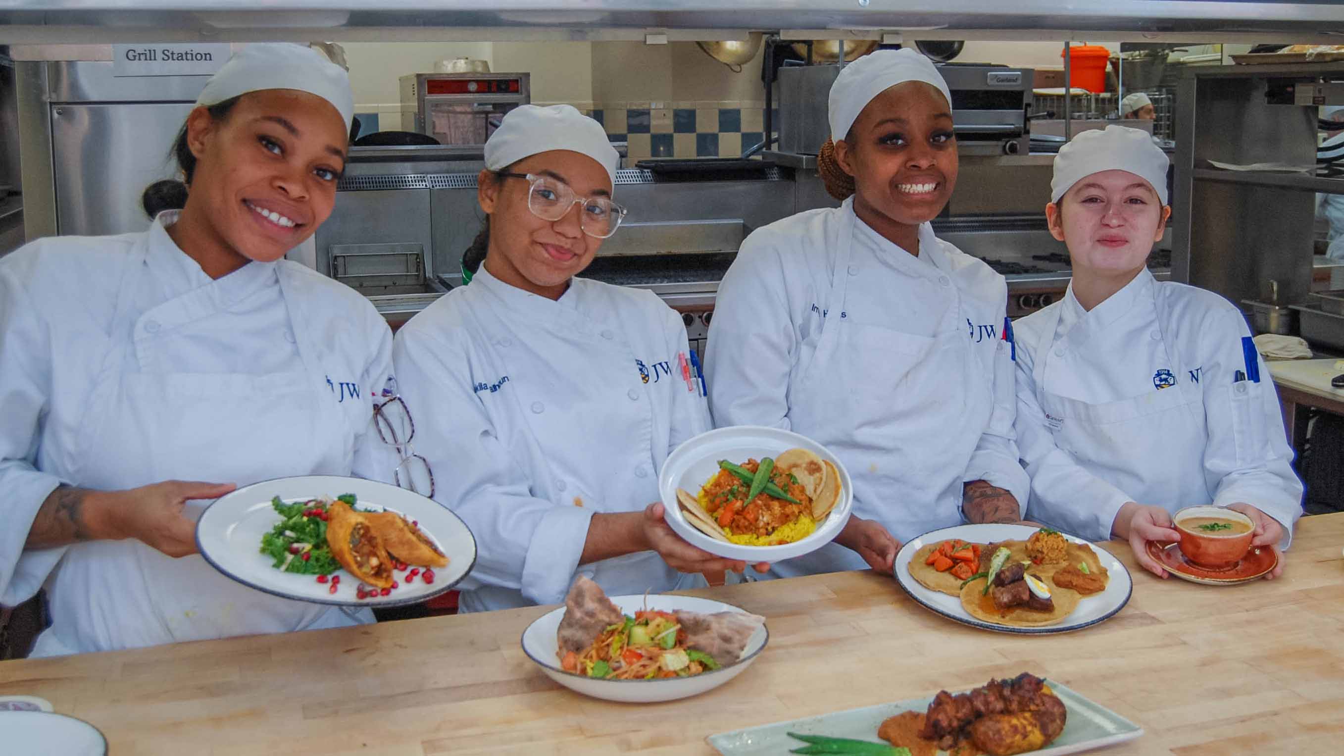 Culinary students in white chef hats and coats present final dishes