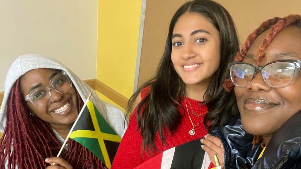 Three students standing together smiling holding their countries flags 